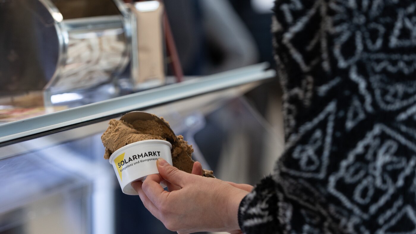Hand einer Frau mit gemusterten Hemd und einem Eis in der Hand | © Swissolar / Sarah Bollmann, atelier olive GmbH